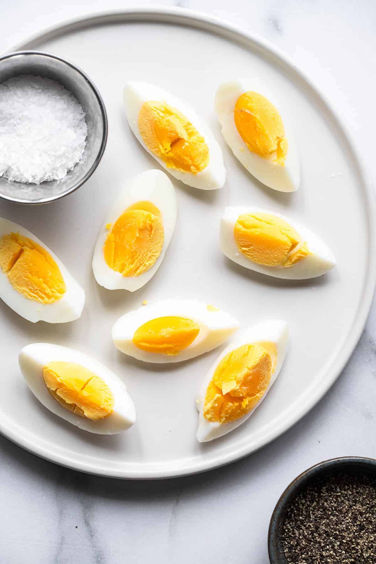sliced air fryer hard boiled eggs on a plate with a bowl of salt