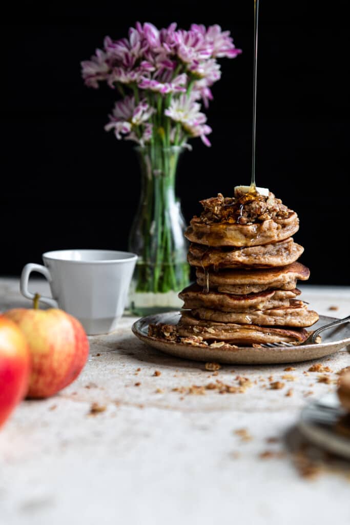healthy apple pancakes in the background on a table with flowers and a teacup