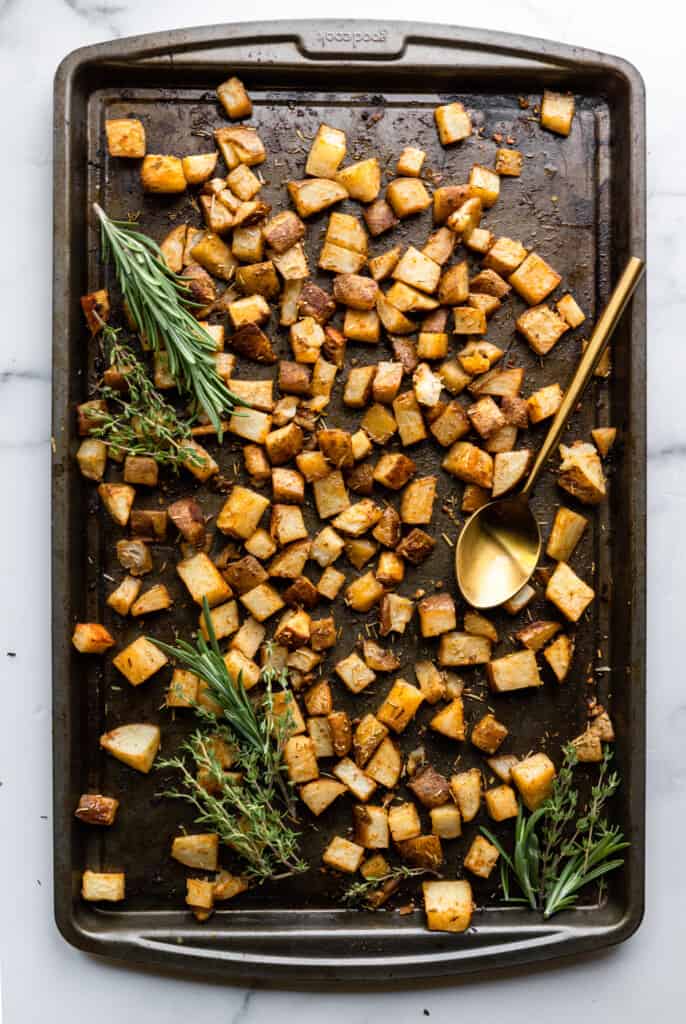 Roasted Russet Potatoes on a backing sheet with a spoon and rosemary